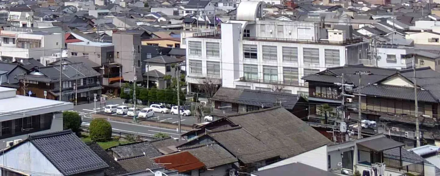 福知山市の中心部を高い所から見た風景。瓦やスレートの屋根の家や店が並び、中ほどに白いビル