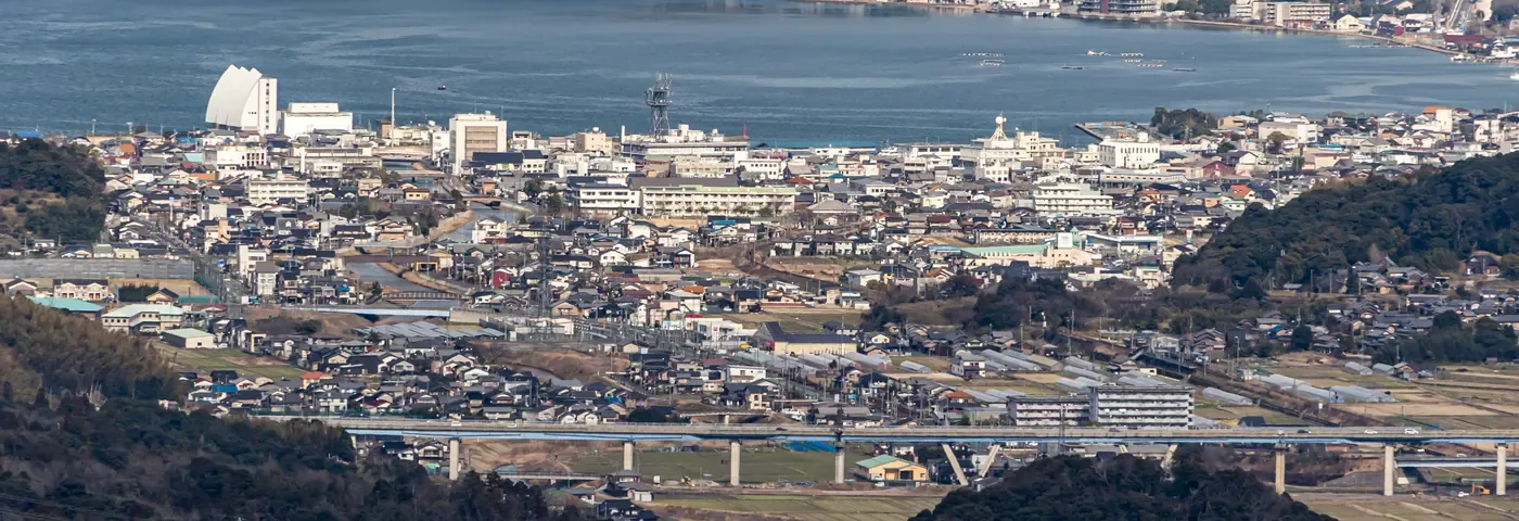 宮津市の中心街を山の上から見下ろした風景。瓦屋根の家が密集した市街地と高架道路、奥に宮津湾