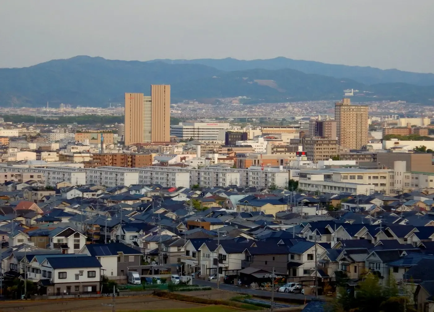 高台から見た長岡京市の市街地。手前に戸建て住宅の屋根が密集し、奥に集合住宅と高層ビル、山並み