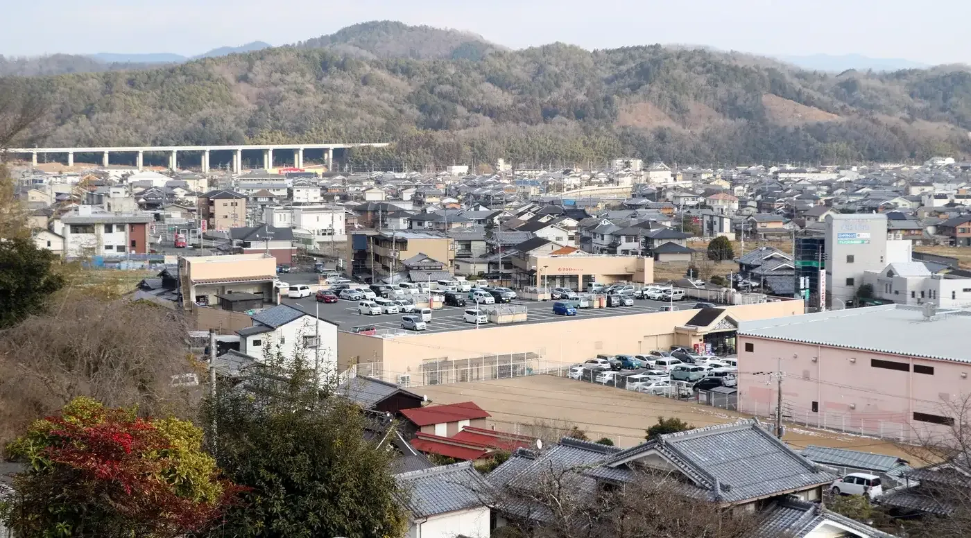 南丹市園部町の町並みを高台から見た風景。瓦やスレートの屋根の家が広がり、奥に高架橋と山並み