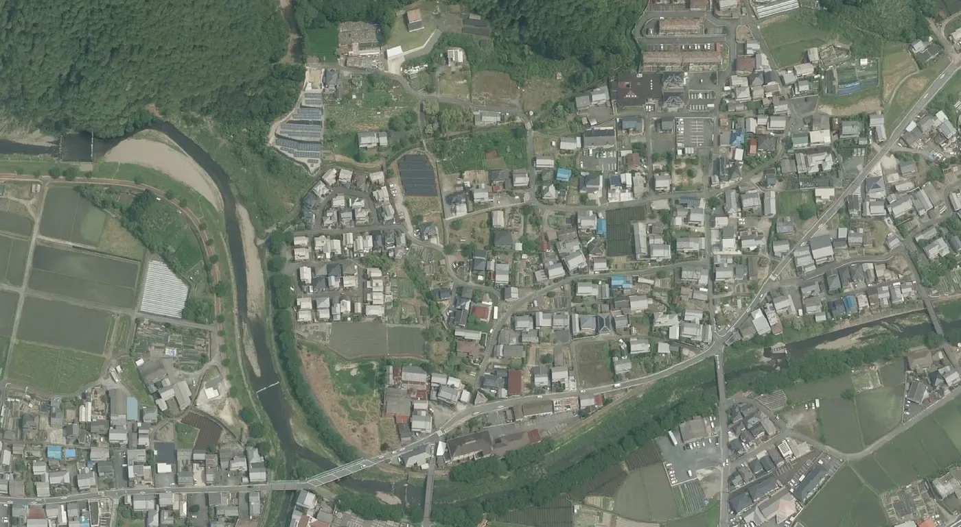 宇治田原町の中心部の住宅地を真上から見た空中写真。山すそに一戸建ての屋根が並び、左に川と田んぼ