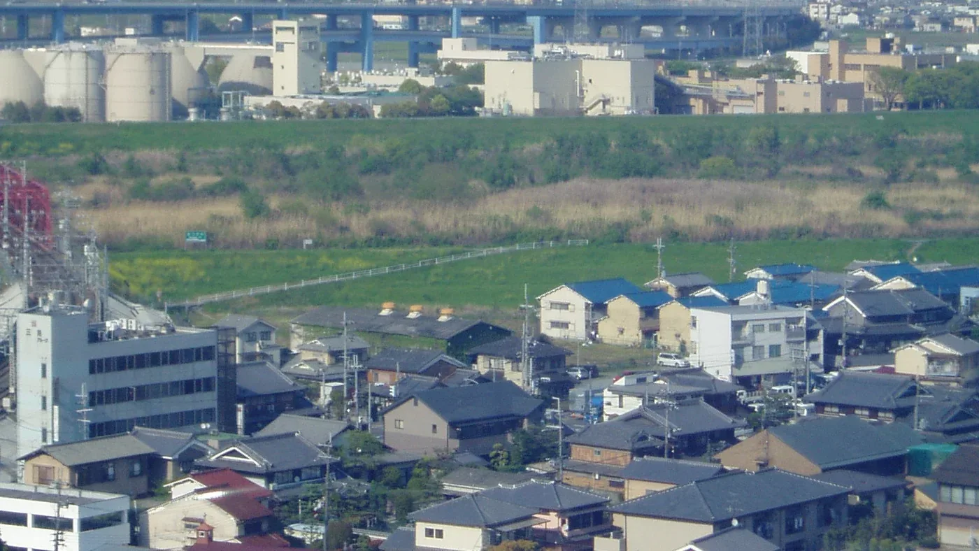 男山から見下ろした八幡市の住宅地。手前に瓦屋根の戸建てが並び、その先に川の堤防と河川敷、左に赤い鉄橋